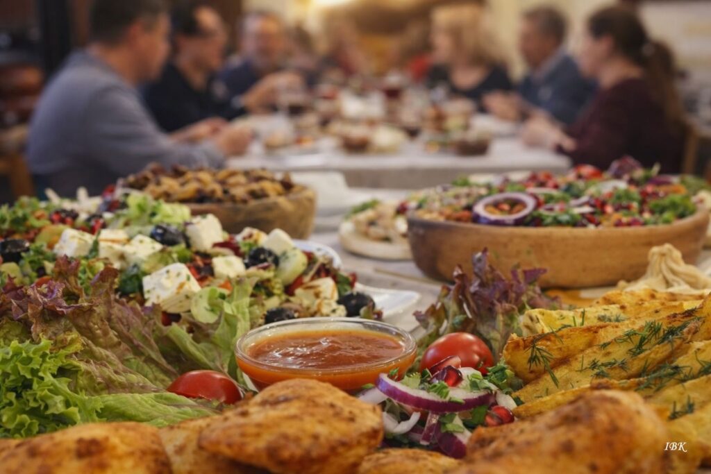 Große georgische Tischtafel mit verschiedenen Salaten, Brotgebäck, roter Sauce und Menschen beim gemeinsamen Essen.